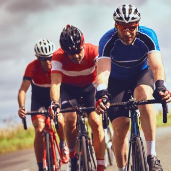 Tre män som cyklar på landsvägscyklar och ligger nära varandra i en klunga.